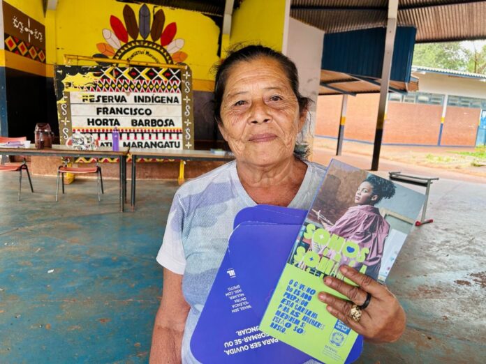 Cidadania faz encontro em territórios para discutir atendimento às mulheres Anciã indígena da etnia guarani com cartazes da campanha de enfrentamento à violência contra a mulher.